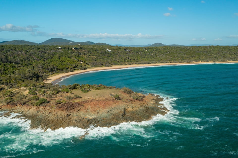 A coastal landscape with a beach, rocky outcrops, and a forested hill.