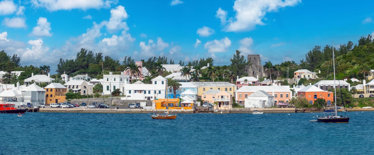 A coastal town with colorful buildings, a dock with boats, and a church in the background.