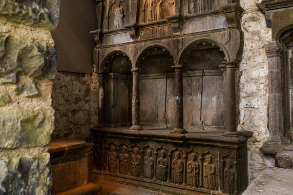 A stone wall with carved figures and a wooden structure with arched niches.
