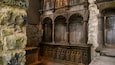 A stone wall with carved figures and a wooden structure with arched niches.