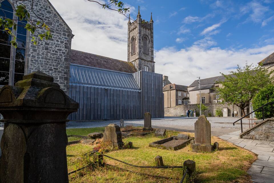 Una iglesia histórica con una torre alta, muros de piedra y un cementerio con lápidas.