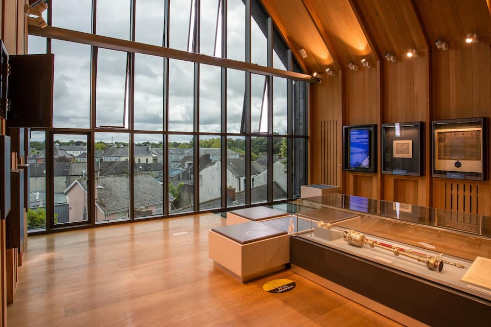 Interior de museu amb finestres grans, parets de fusta i exposicions, incloent-hi una peça d'artfacte daurada.