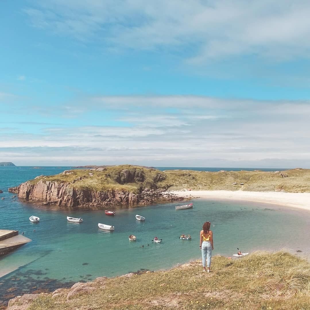 A coastal landscape with a sandy beach, rocky outcrops, and clear turquoise waters.