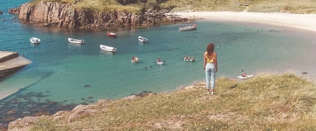 A coastal landscape with a sandy beach, rocky outcrops, and clear turquoise waters.