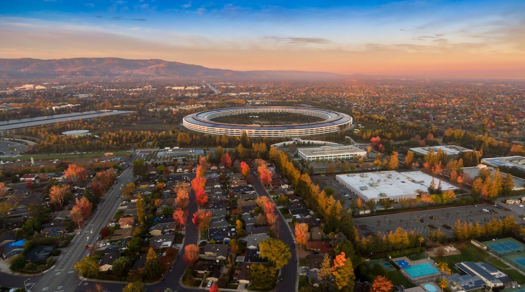 Aerial view of Apple Park headquarters in Santa Clara, California, USA. The circular building is surrounded by trees in autumn colors at sunset.