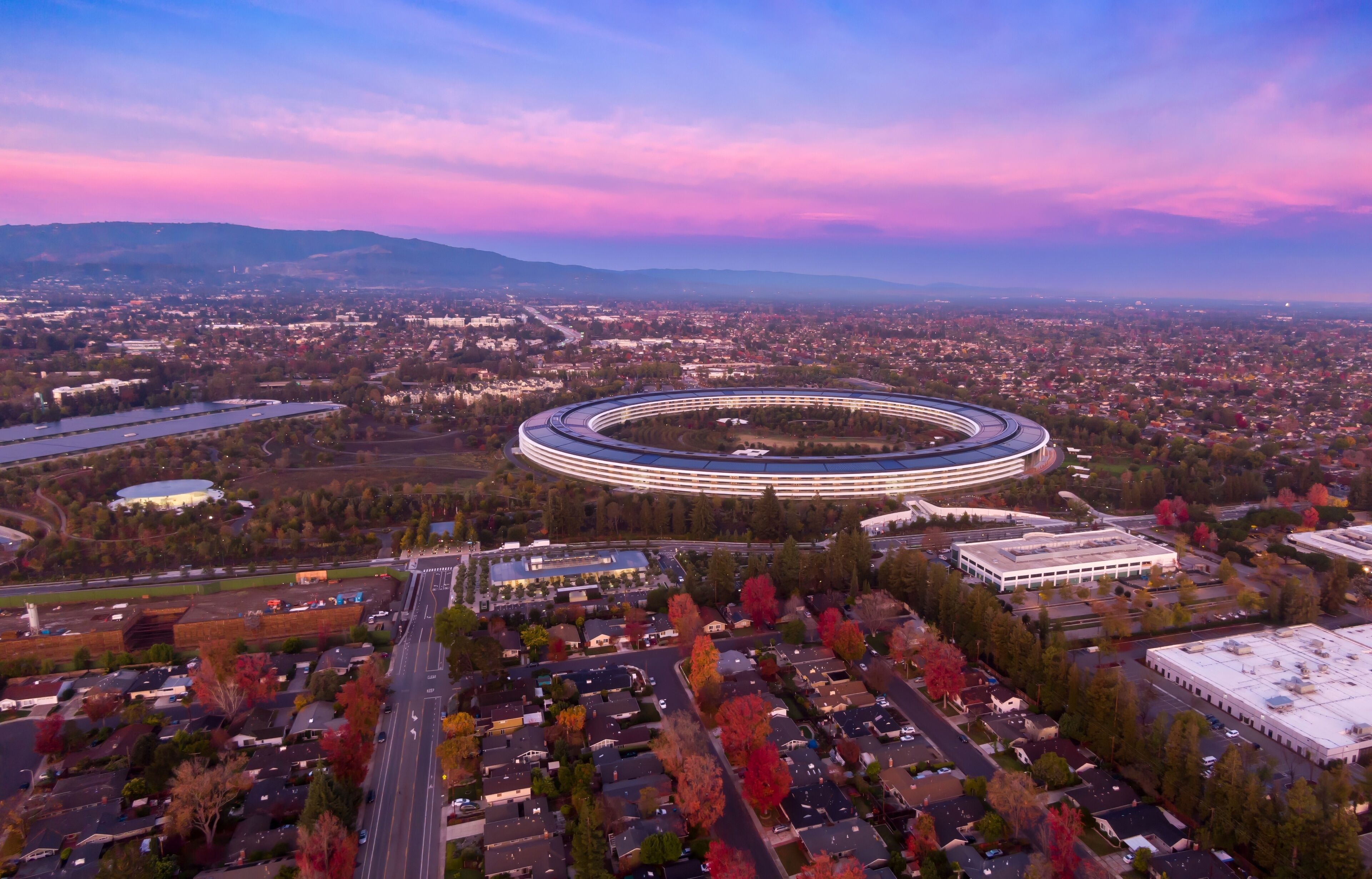Aerial view of Apple Park headquarters in Santa Clara, California, USA, at sunset. The circular building houses Apple employees and promotes innovation.