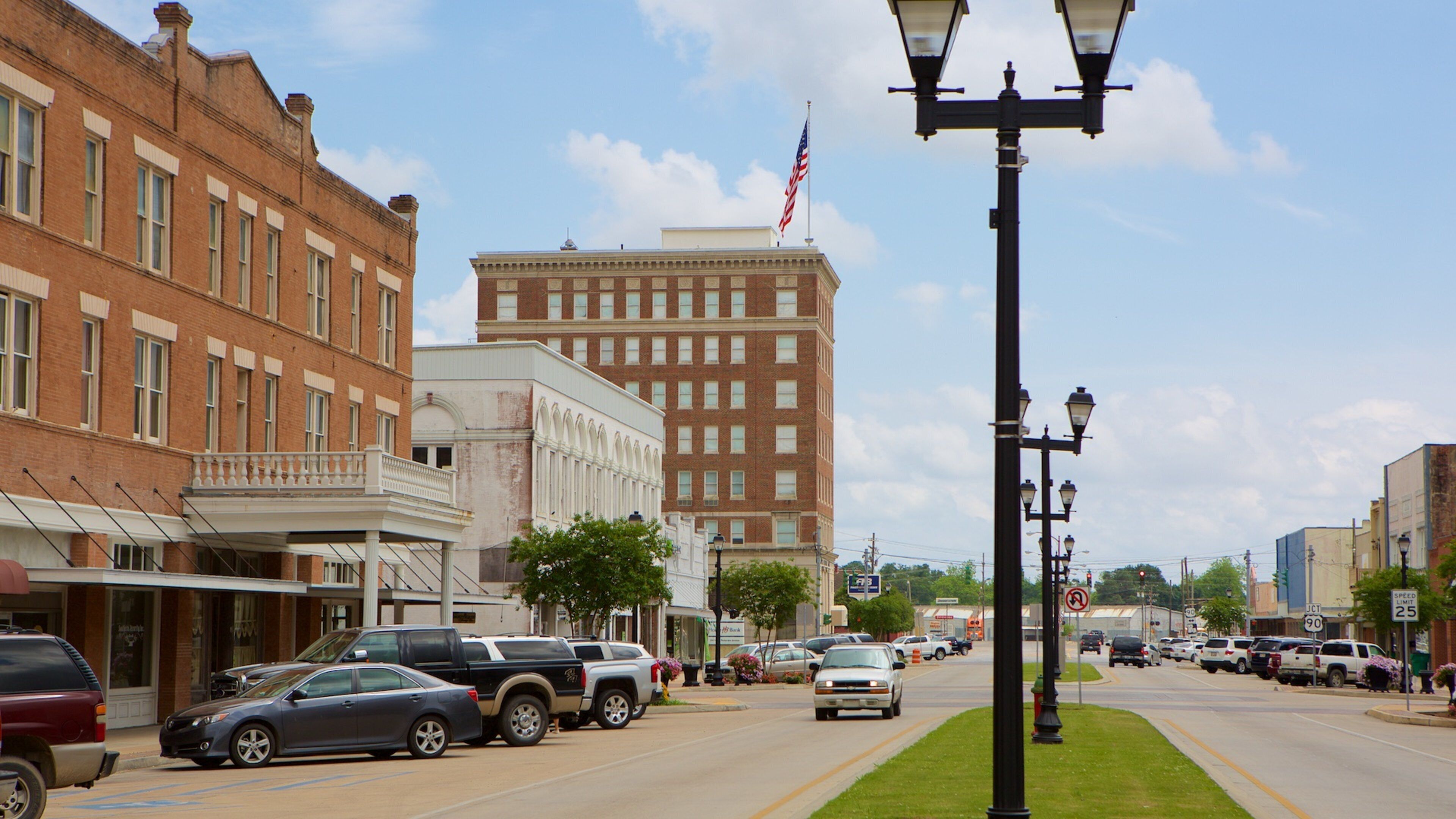 A street lined with historic buildings, parked cars, and a prominent American flag.