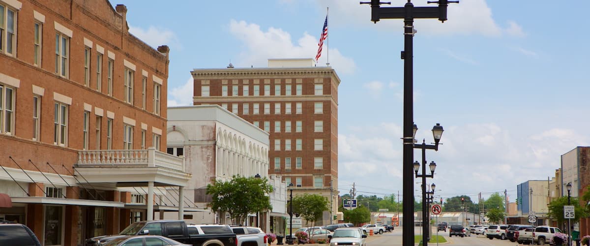 A street lined with historic buildings, parked cars, and a prominent American flag.