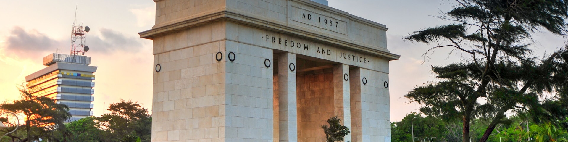 Un monumento con inscripciones 'AD 1957' y 'FREEDOM AND JUSTICE', coronado por dos estrellas, rodeado de follaje.