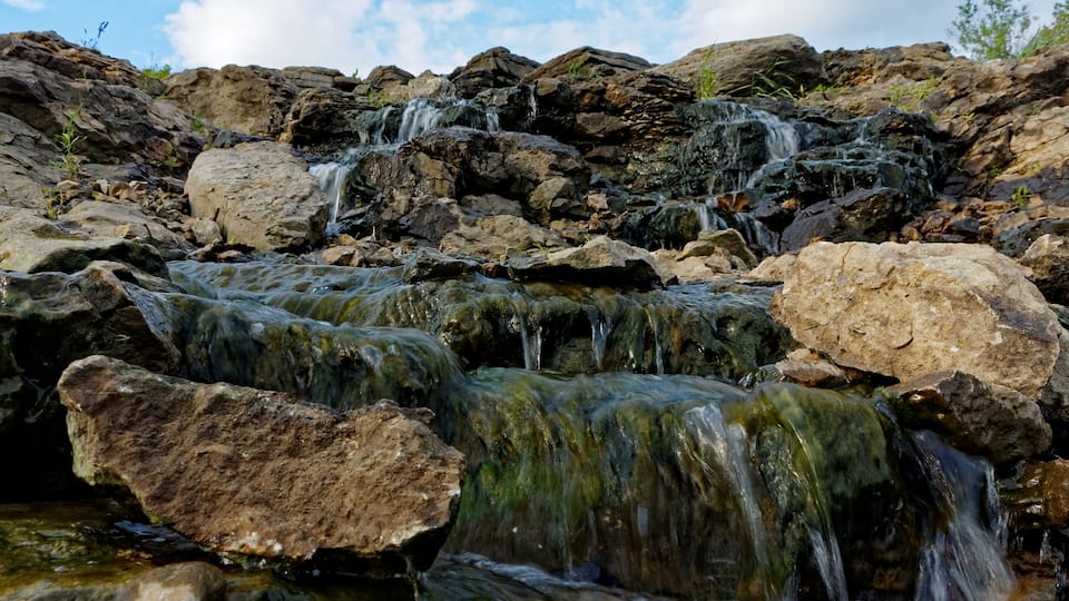 The water rushes over the Lake MacBride Waterfall. This waterfall has several main falls and numerous smaller falls.