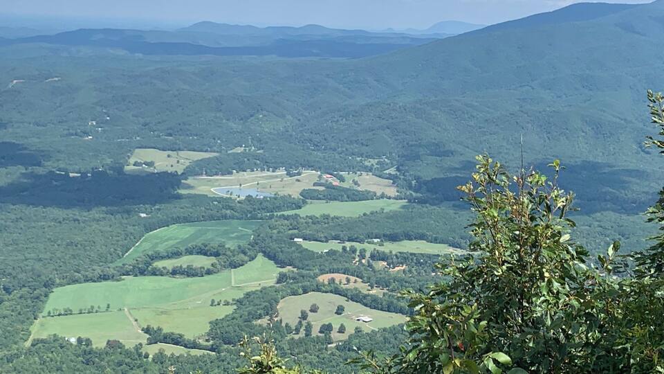 A mountainous landscape with rolling hills, scattered fields, and a river.