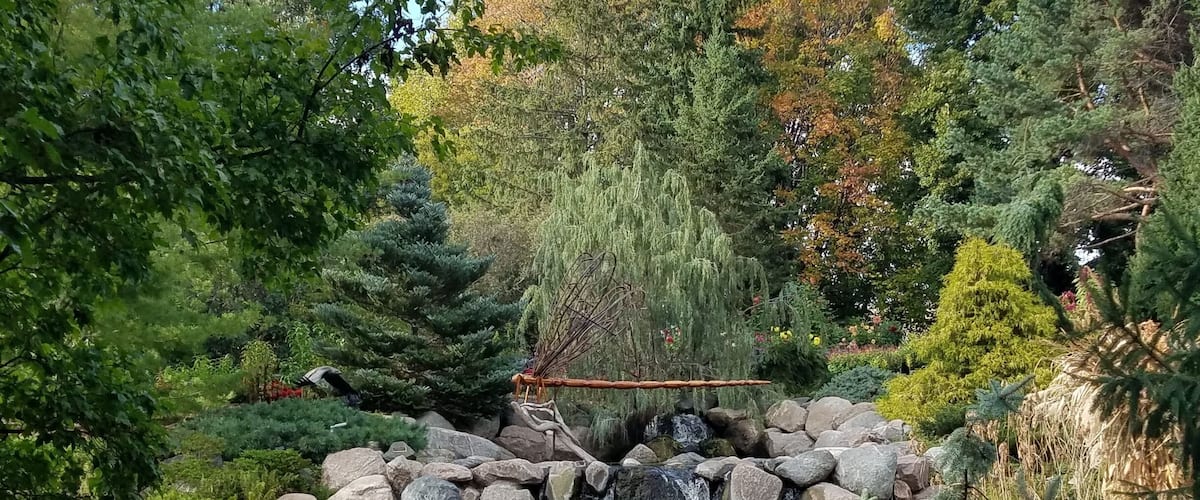 A serene garden with a small waterfall, large rocks, and lush greenery.