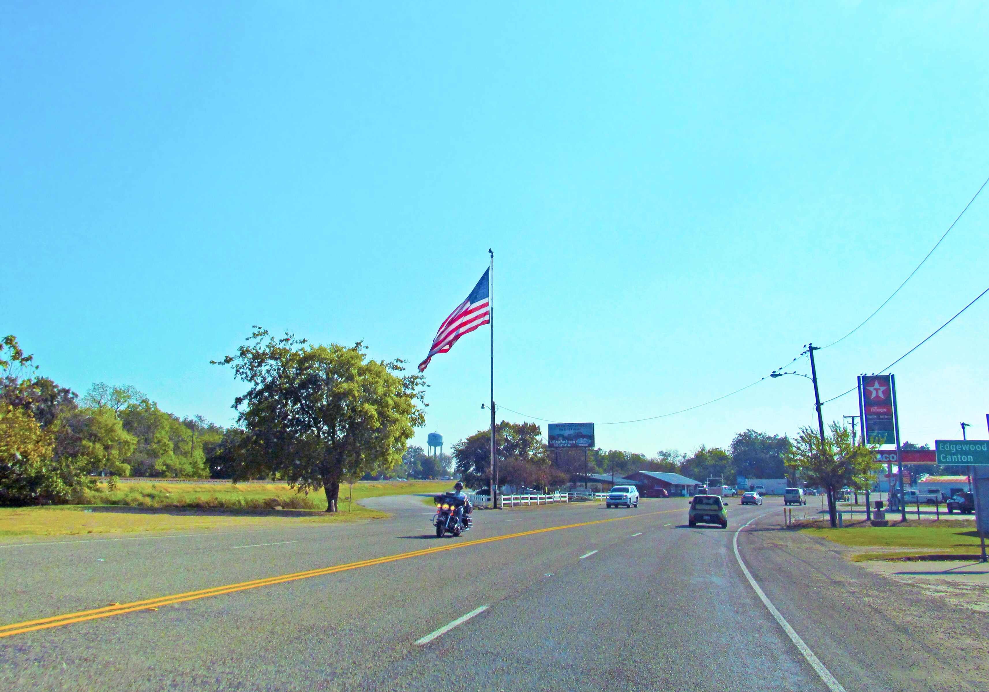 Canton, TX, USA - October 14, 2017: Rider biker on motorcycle, cars on the road and a American flag. Traffic in a countryside near Canton in Texas in summer sunny day.