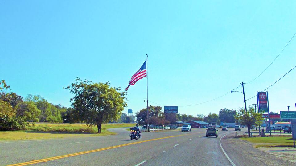 A highway with a large American flag, a motorcyclist, and a Texaco gas station.