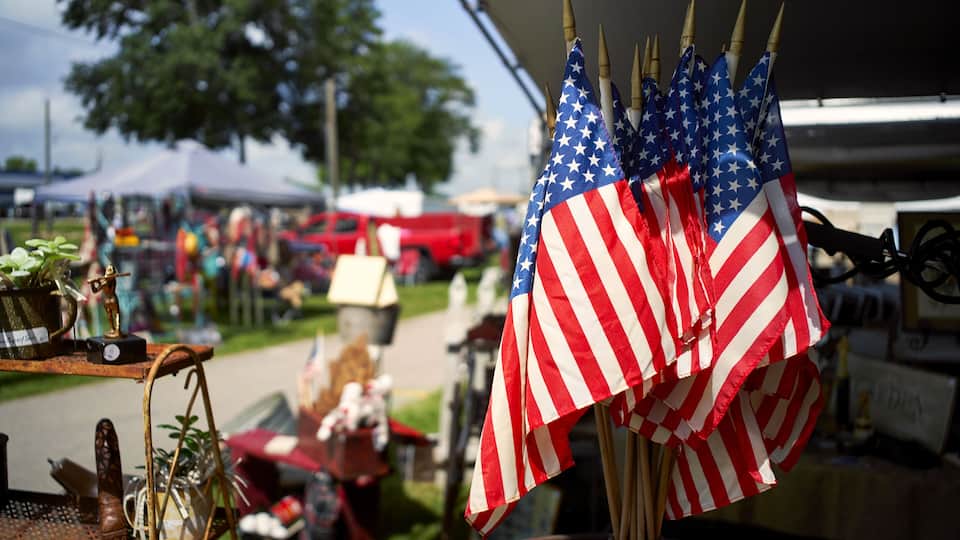 A collection of American flags and a vintage radio on a table at an outdoor market.