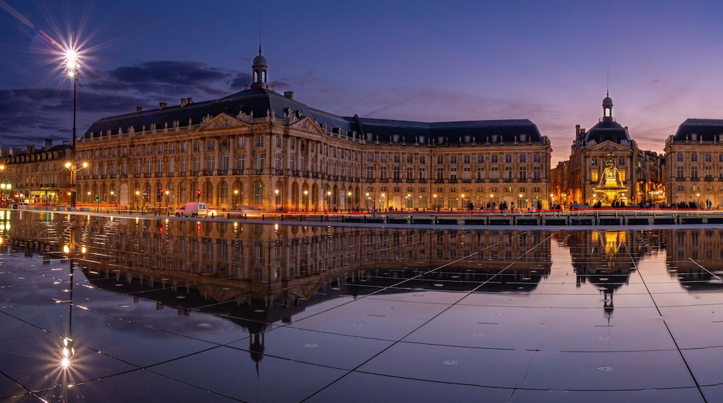 A grand building with a central dome, flanked by two symmetrical wings, reflecting in a calm water surface.