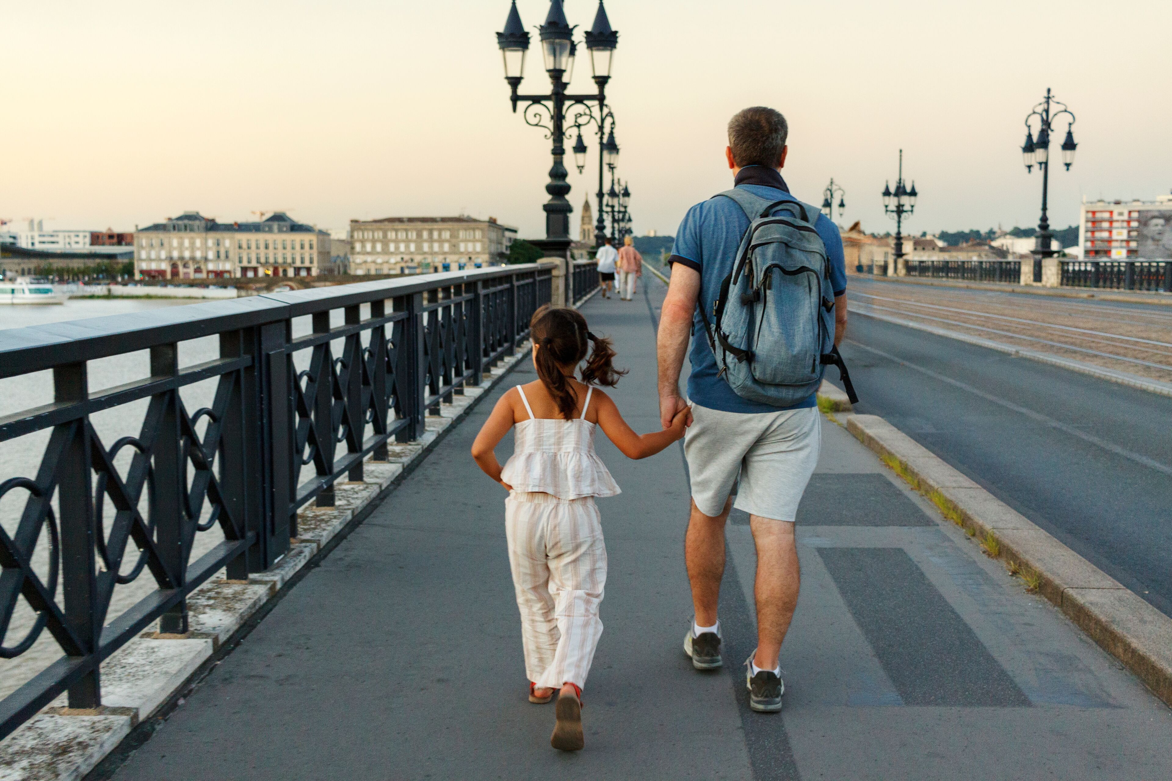 Una pareja caminando sobre un puente, con un río y edificios al fondo.