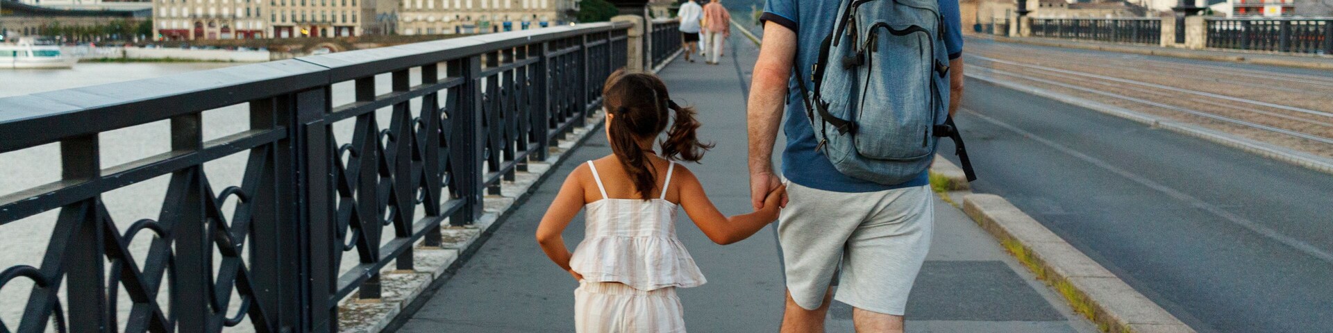 Um casal caminhando sobre uma ponte, com um rio e edifícios ao fundo.