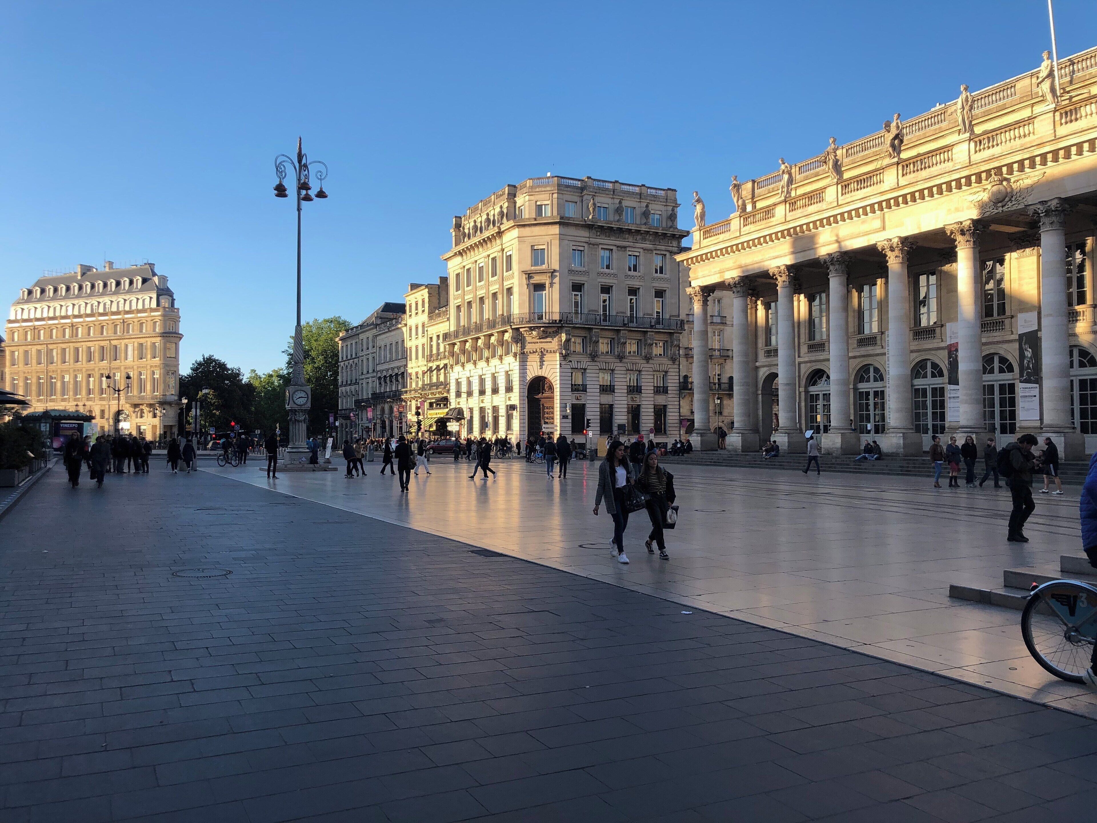 Una plaza amplia y abierta con edificios históricos, una torre del reloj y gente caminando.