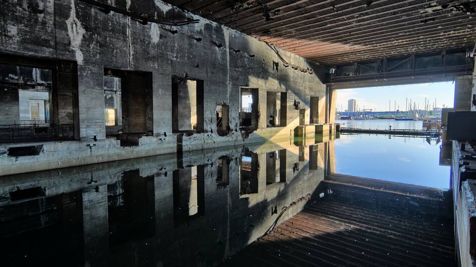 An abandoned industrial building with large windows and a view of a marina.