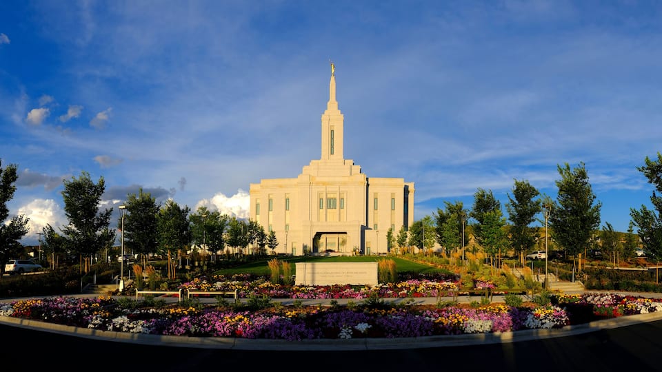 A large building with a tall spire, surrounded by a landscaped garden with various colorful flowers.