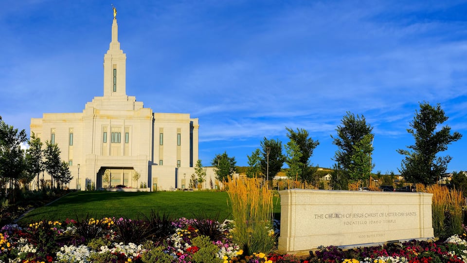 A church with a tall steeple, surrounded by colorful flowers and trees.