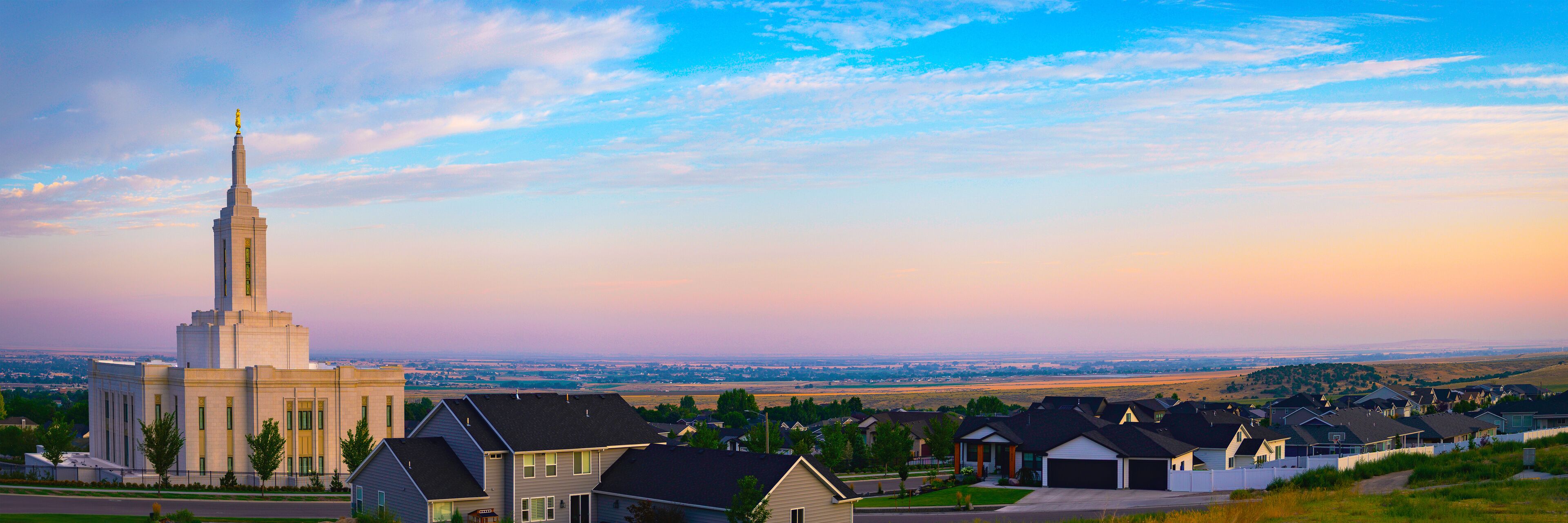 A large white church with a tall steeple, surrounded by residential houses and a wide-open landscape.