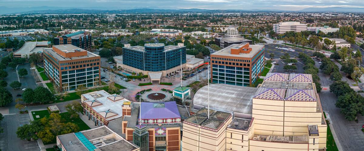 An aerial view of a cityscape with modern buildings, a central plaza, and surrounding greenery.