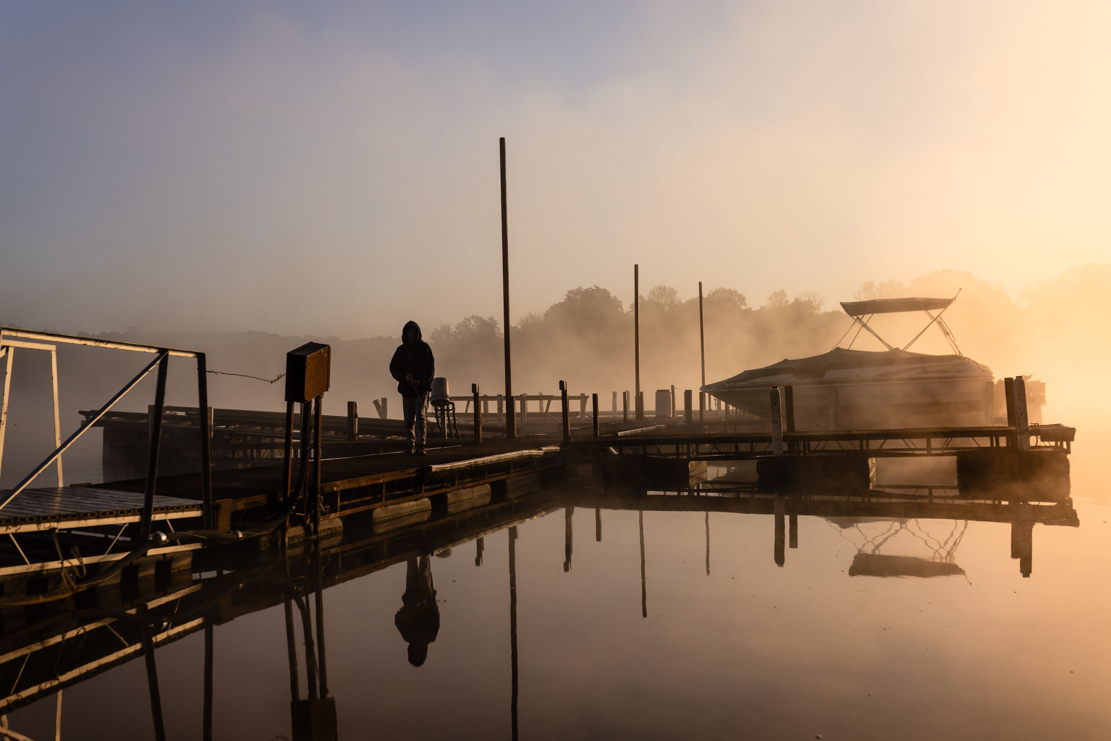 Un puerto brumoso con un muelle, una persona de pie sobre el muelle y un barco con cabina.