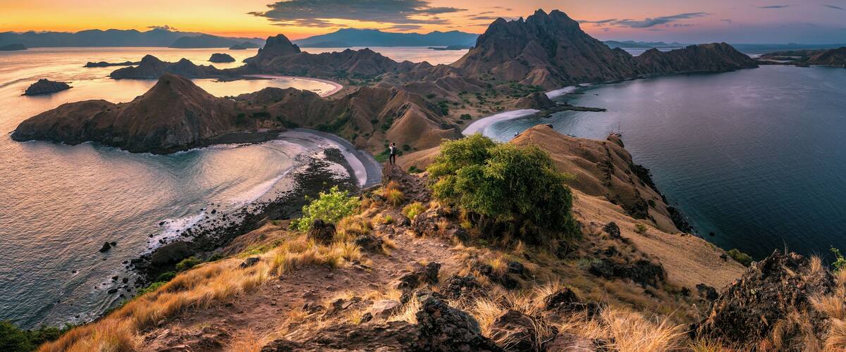 A coastal landscape with rugged mountains, a winding road, and a body of water.