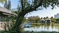 A serene lake with blue boats, a traditional pavilion, and modern buildings in the background.
