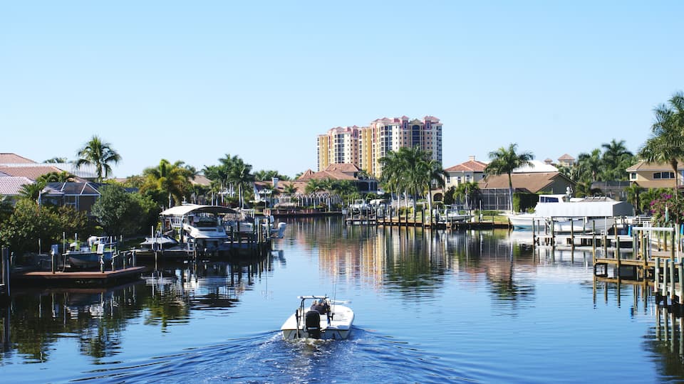 A marina with boats, a waterway, and residential buildings with palm trees.