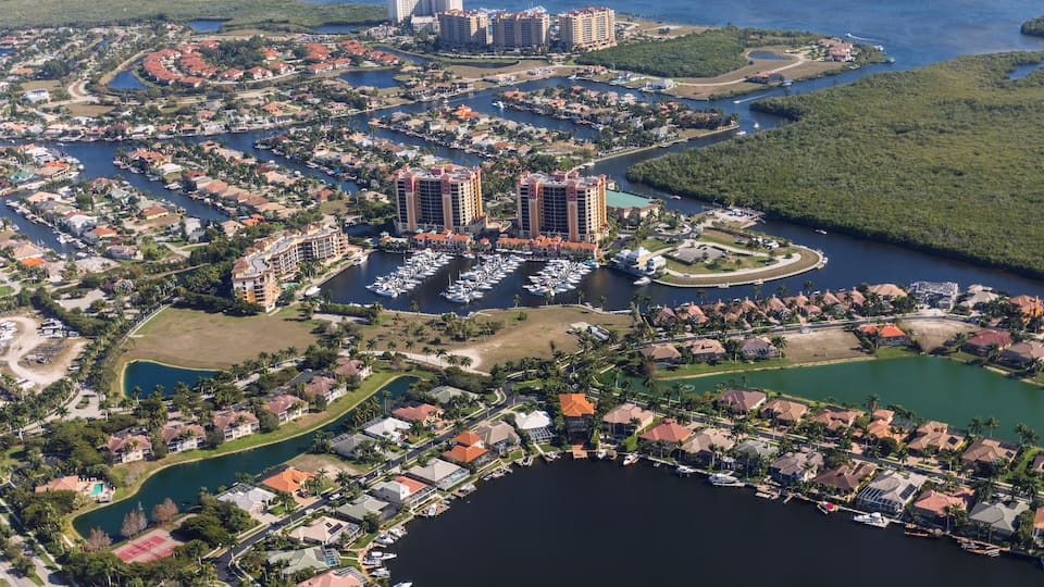An aerial view of a coastal residential area with multiple buildings, a marina, and surrounding water bodies.