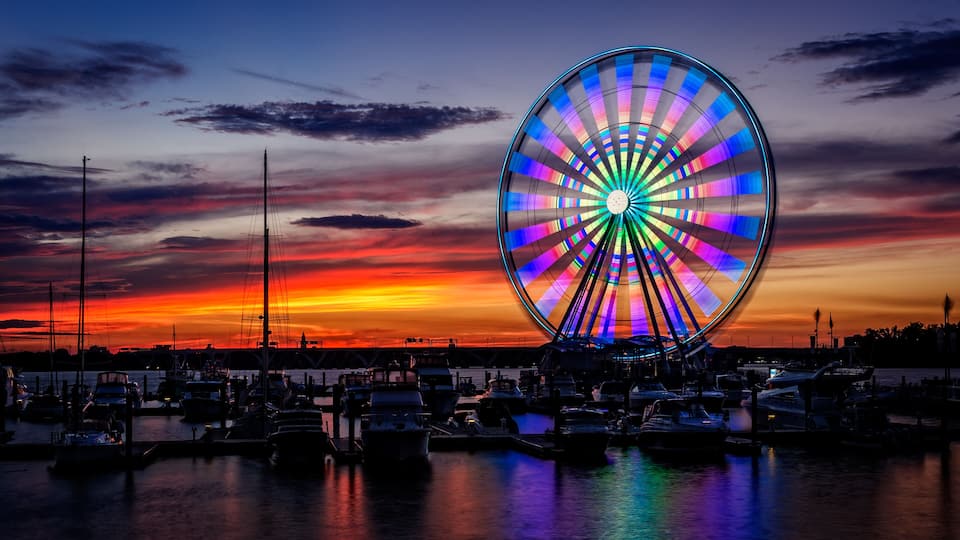 A vibrant sunset with a colorful Ferris wheel and a marina filled with boats.