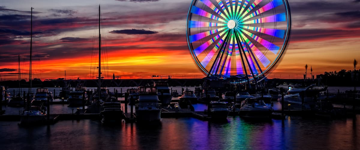 A vibrant sunset with a colorful Ferris wheel and a marina filled with boats.