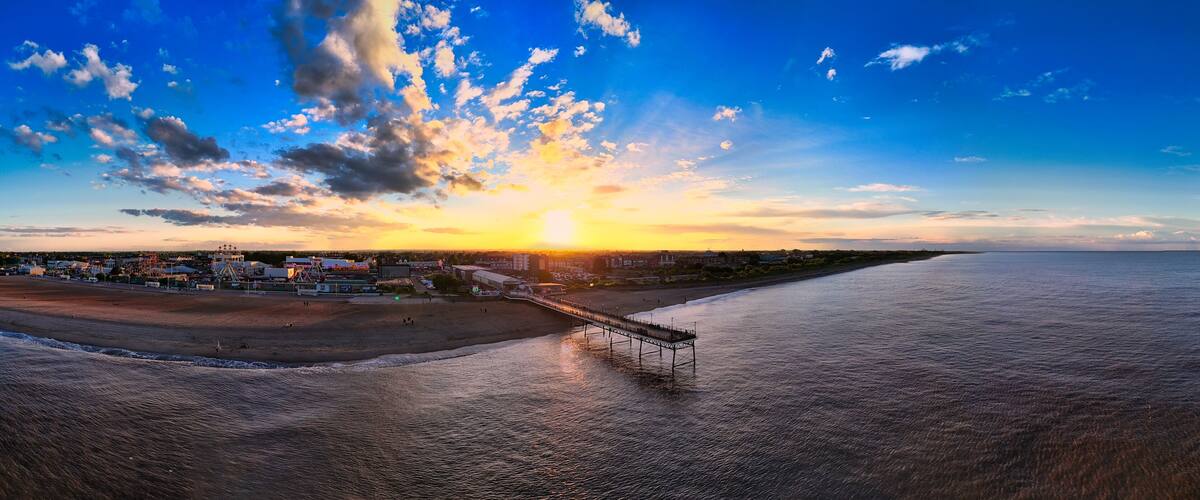 A sunset over a beach with a pier extending into the water.