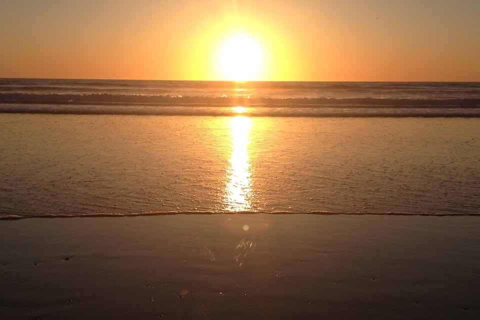 A sunset over a beach with waves and a clear sky.