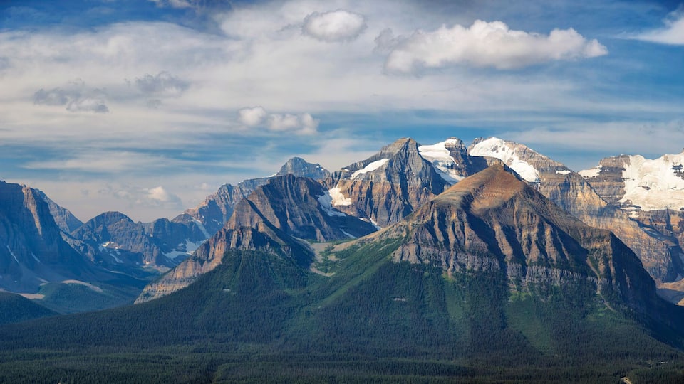 A mountain range with snow-capped peaks and a valley with dense forests.