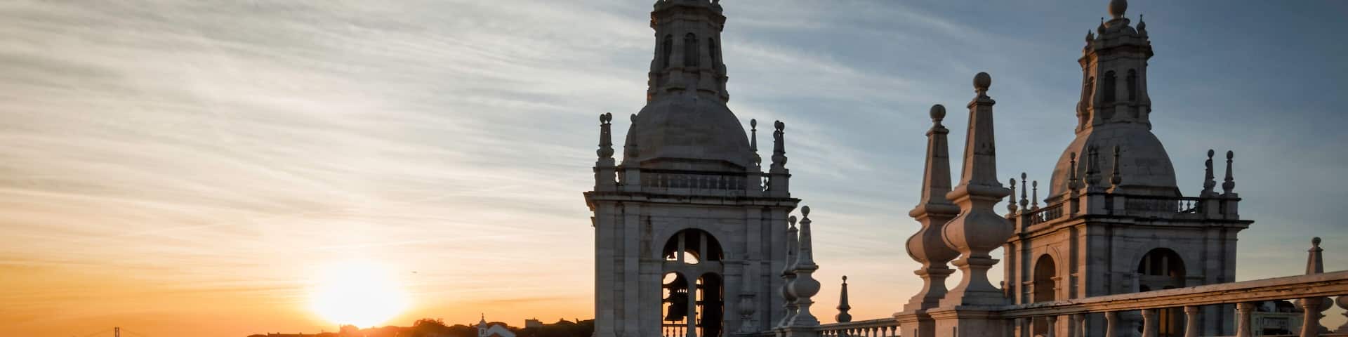 A historic cathedral with two prominent towers and a dome, set against a sunset sky.