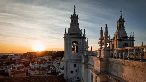 A historic cathedral with two prominent towers and a dome, set against a sunset sky.