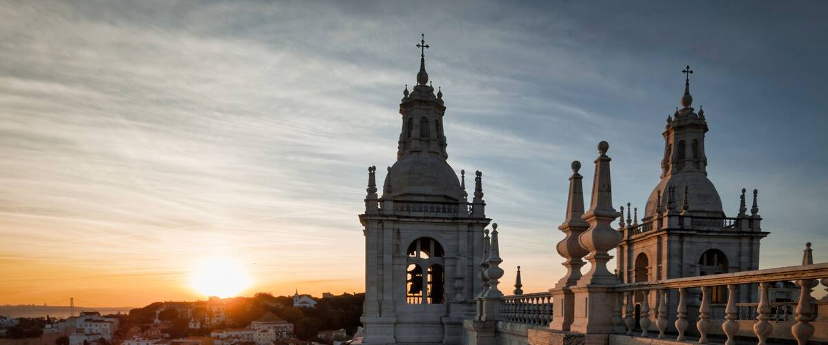 A historic cathedral with two prominent towers and a dome, set against a sunset sky.