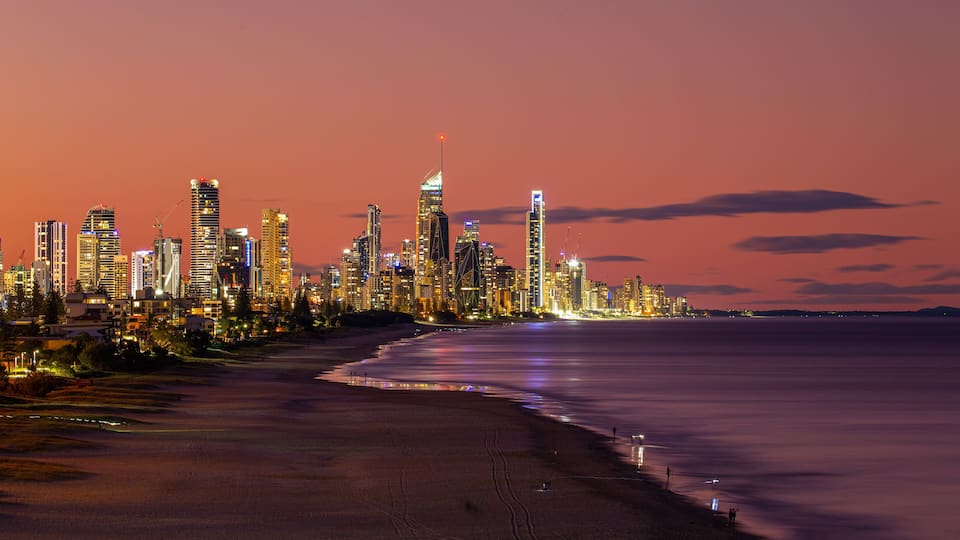 A city skyline at dusk with illuminated buildings and a beach in the foreground.