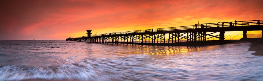 Un muelle se adentra en el océano al atardecer, bajo un cielo vibrante.