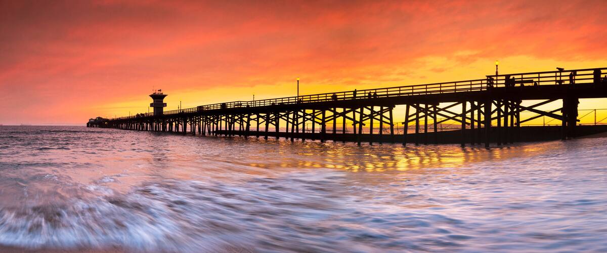 A pier extending into the ocean at sunset with a vibrant sky.