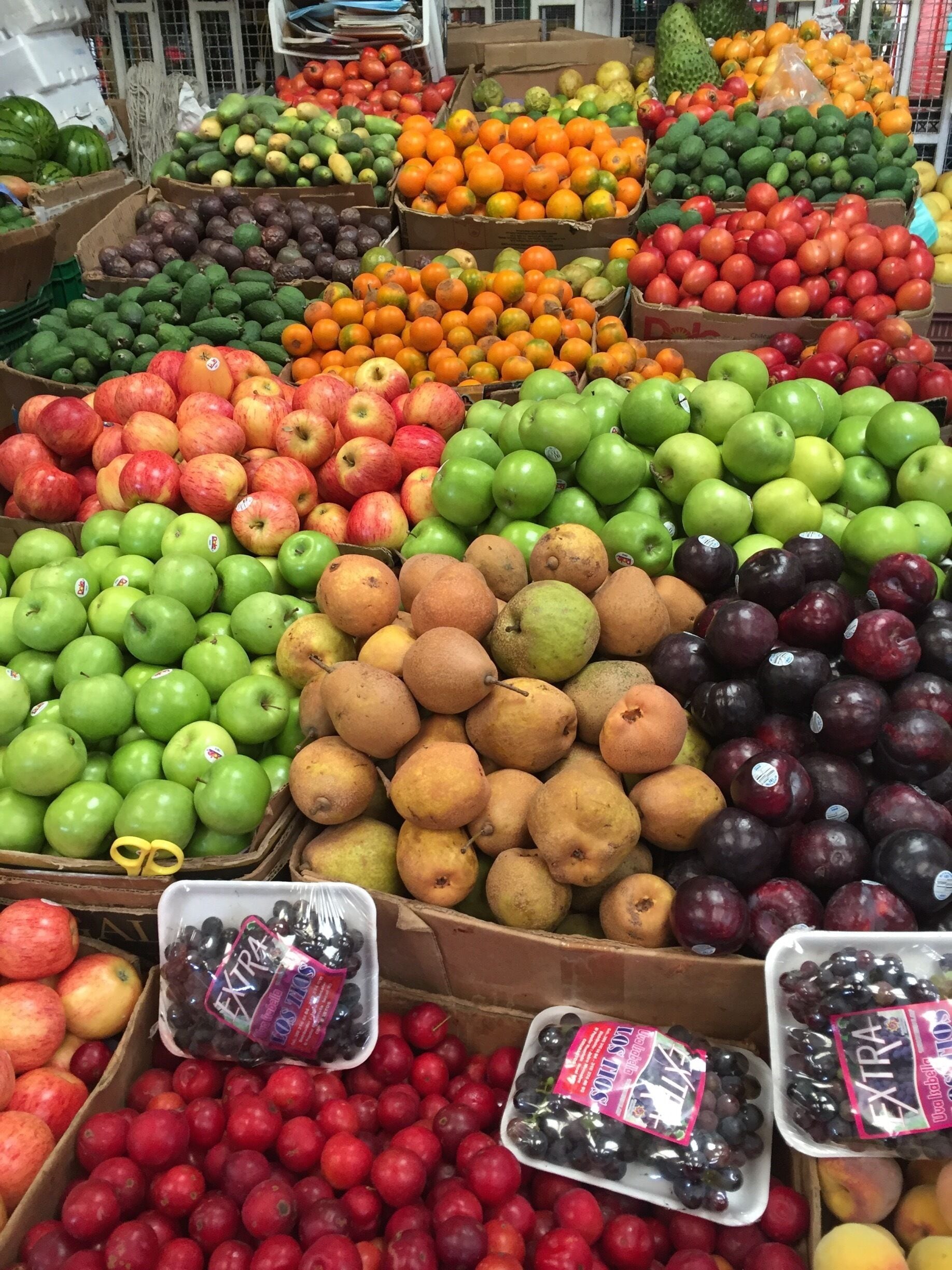Uma banca de mercado com diversas frutas, como maçãs, peras, ameixas e laranjas.