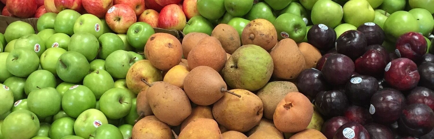 Uma banca de mercado com diversas frutas, como maçãs, peras, ameixas e laranjas.