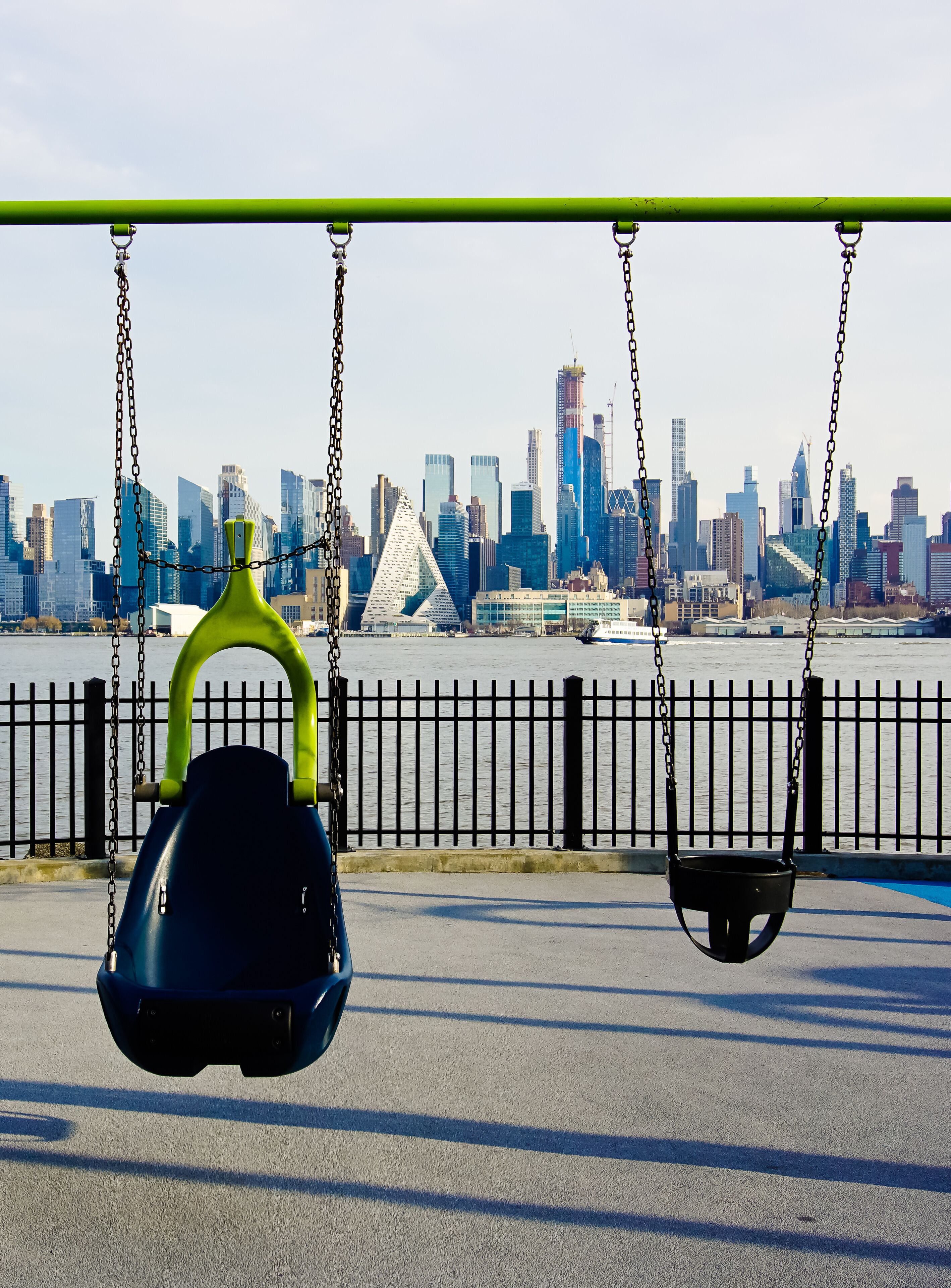A park with swings, a waterfront, and a city skyline in the background.