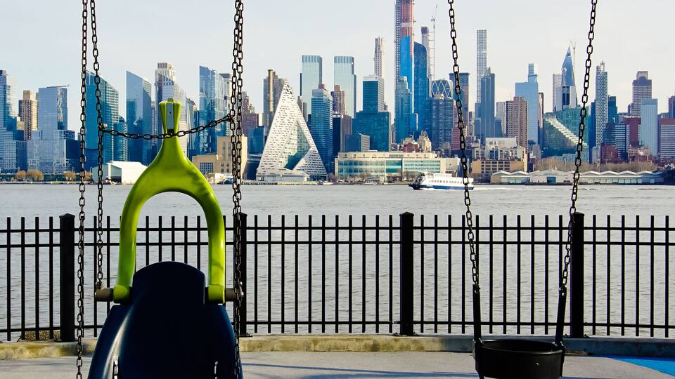 A park with swings, a waterfront, and a city skyline in the background.