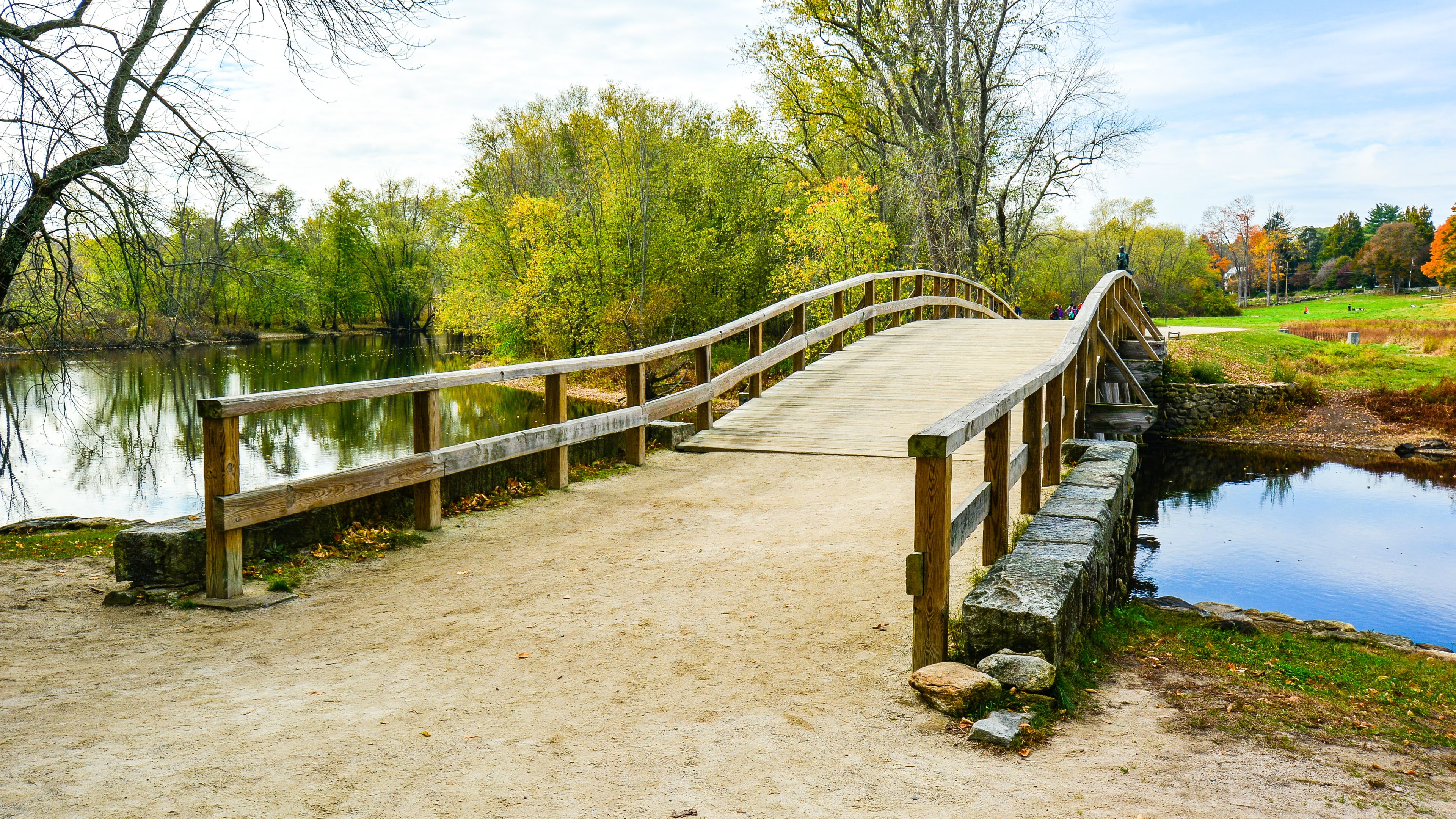 A wooden bridge over a calm river, surrounded by trees and grassy areas.