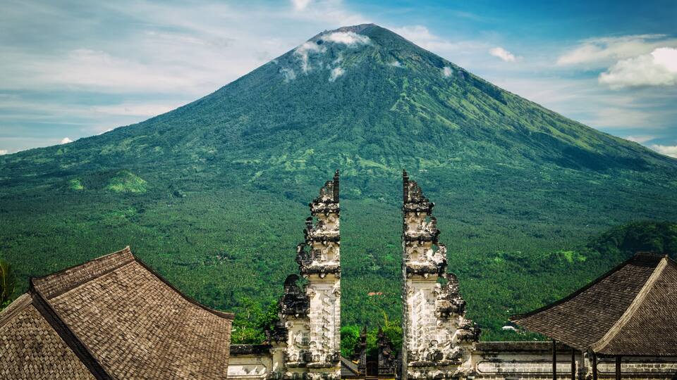 A temple with two ornate gateways in front of a lush green mountain.